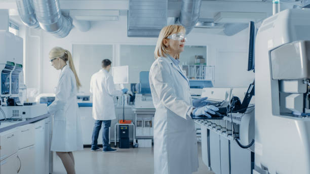 Team of Research Scientists Working On Computer, with Medical Equipment, Analyzing Blood and Genetic Material Samples with Special Machines in the Modern Laboratory.